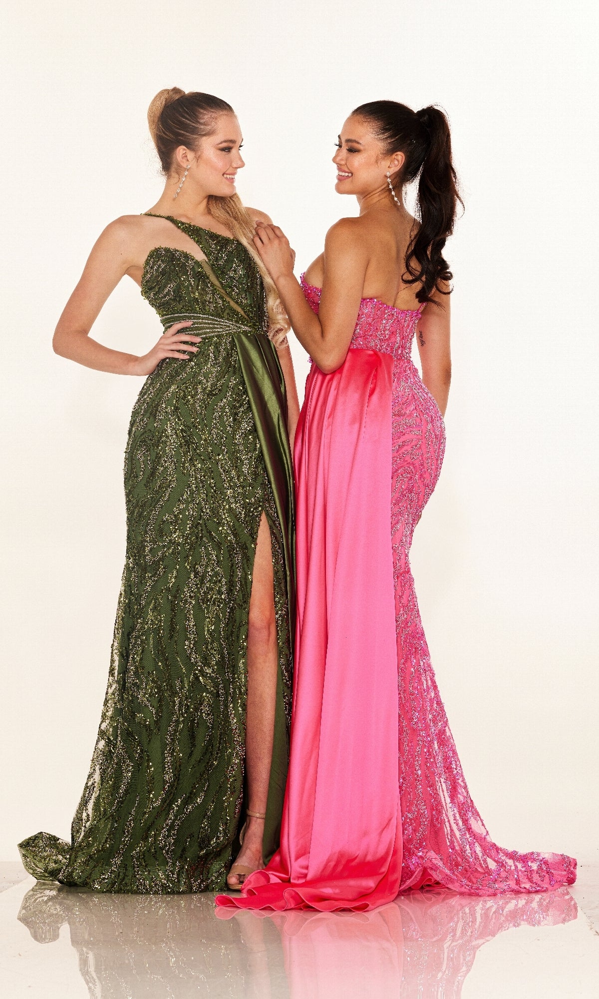Two women stand together, smiling warmly. One wears the Long Prom Dress: Cecilia Couture C275 in green with a high slit, while the other dons a pink gown with lace accents.